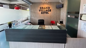 Una reception con una insegna che riporta "Grand Village Hotel" e un orologio appeso al muro.