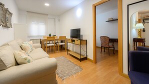En stue med sofa, tv på et træskab, spisebord med stole og et spejl der viser rummet.