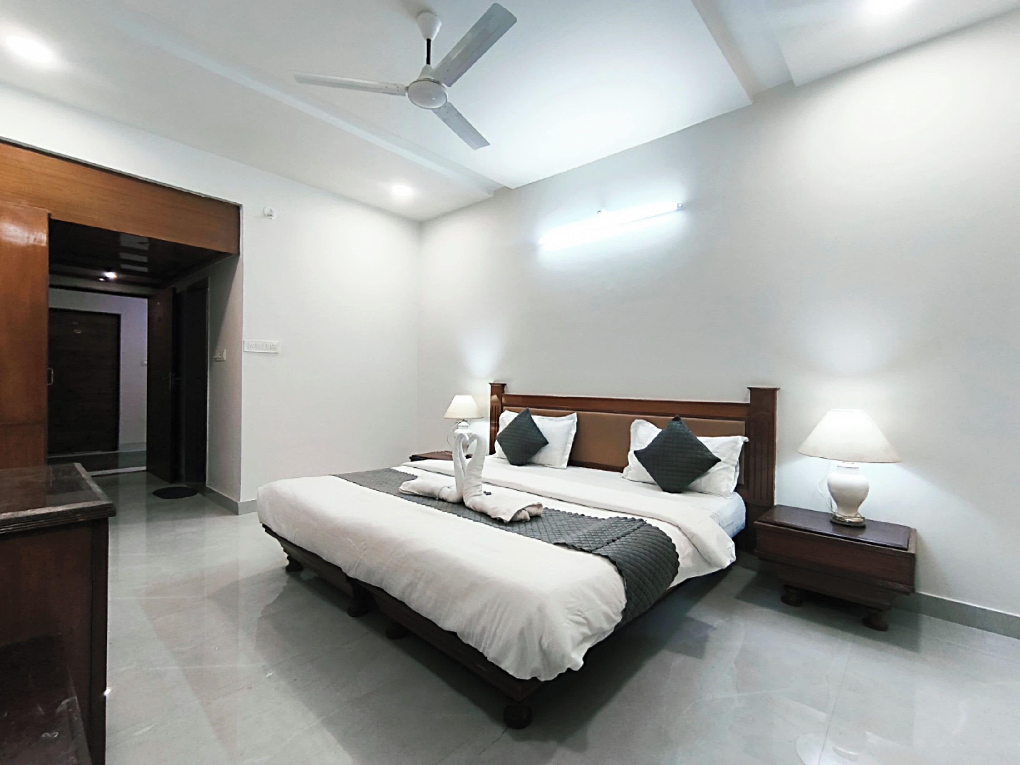 A modern hotel room with a large bed, a ceiling fan, and a nightstand with a lamp.
