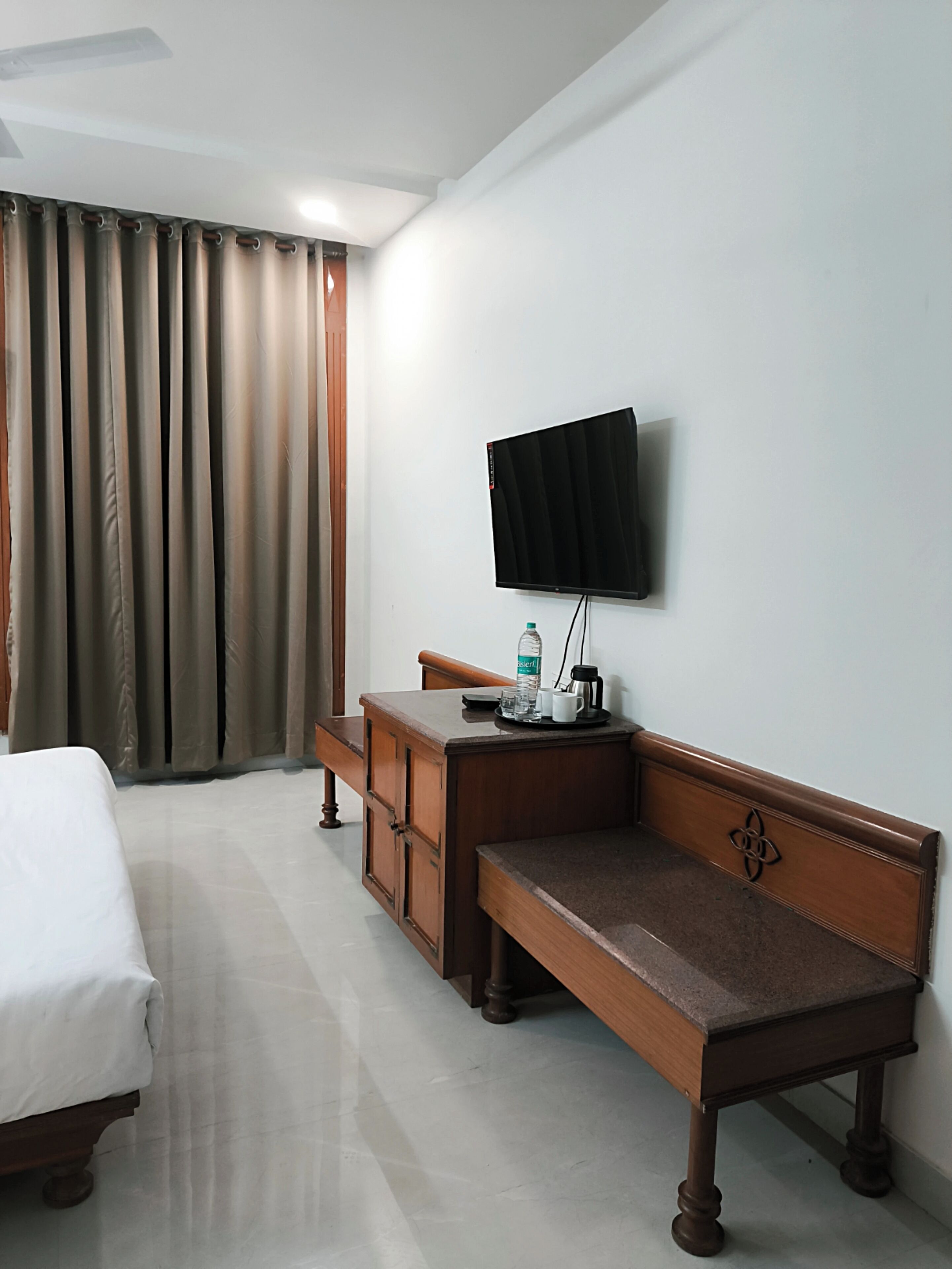 A hotel room with a bed, a desk with a chair, a television mounted on the wall, and a window with curtains.