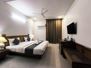 Ein Hotelzimmer mit Bett, Nachttischlampen, Schreibtisch, Fernseher und Deckenventilator.