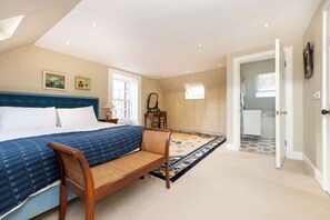 A bedroom with a large bed, a wooden chair, a patterned rug, and a bathroom visible through an open door. - Luxury Family Flat in Edinburgh New Town (Edinburgh)