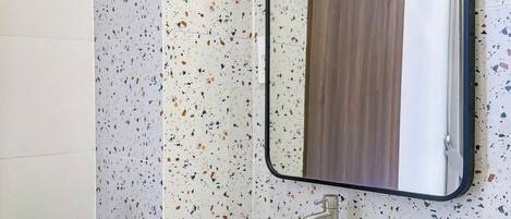 A bathroom with a white sink, a mirror, and a speckled backsplash.