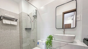 A modern bathroom with a glass-enclosed shower, a white toilet, a white sink with a marble countertop, and a mirror above the sink. - The Cozy Nest 1 – Thao Dien (Ho Chi Minh City)