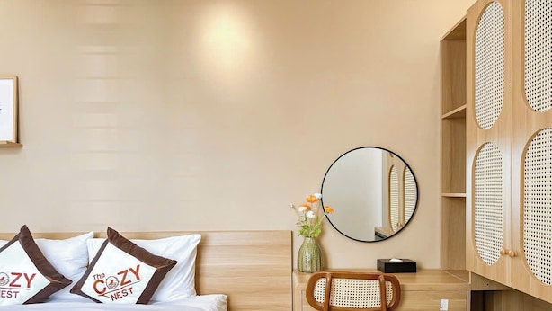 A hotel room with a bed, a desk, a chair, a mirror, and a wall with woven panels. - The Cozy Nest 1 – Thao Dien (Ho Chi Minh City)