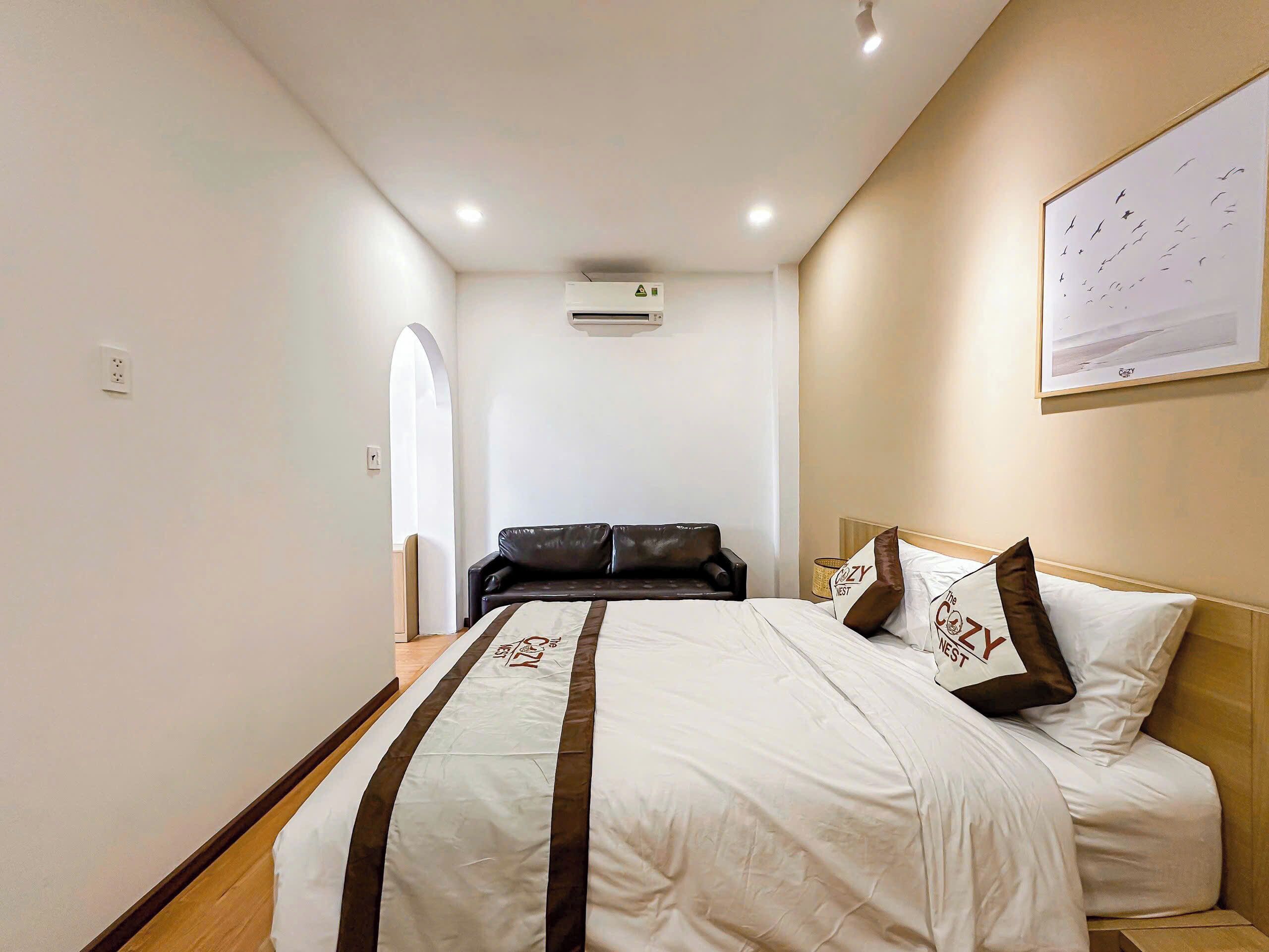 Habitació d'hotel amb un llit, un sofà de pell negra, un aparell d'aire condicionat i una fotografia emmarcada a la paret.