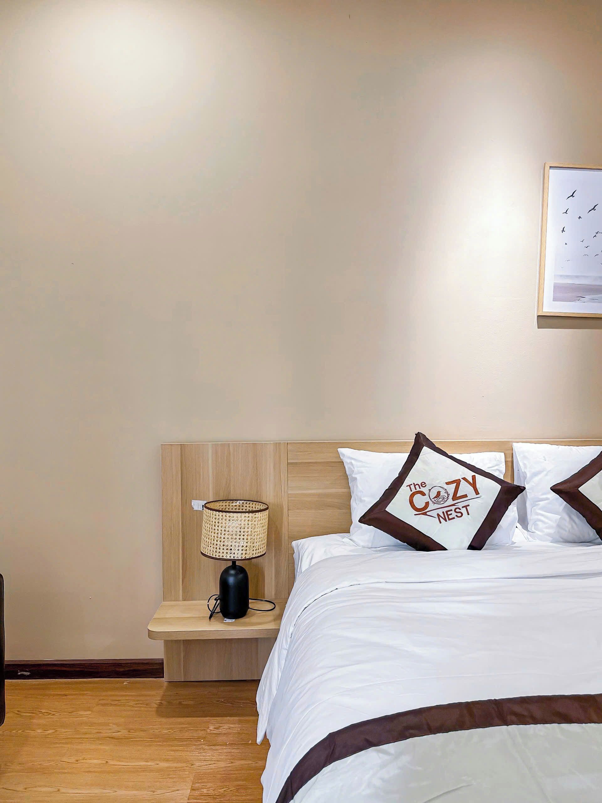 Habitación de hotel impecable con cabecera de madera, mesita de noche con lámpara y cama con ropa blanca y almohadas decorativas.