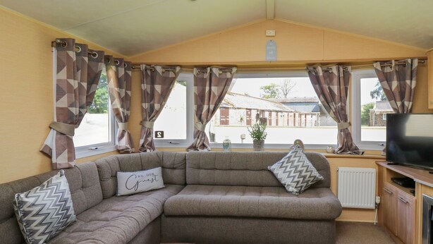 A cozy living area with a sectional sofa, a flat-screen TV, and a view of the outside. - Caravan 2 at Blackmoor Farm Near Tenby (Narberth)