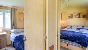 A bedroom with two beds, a wooden wardrobe, a bedside table with a lamp, and a window with curtains. - Caravan 2 at Blackmoor Farm Near Tenby (Narberth)