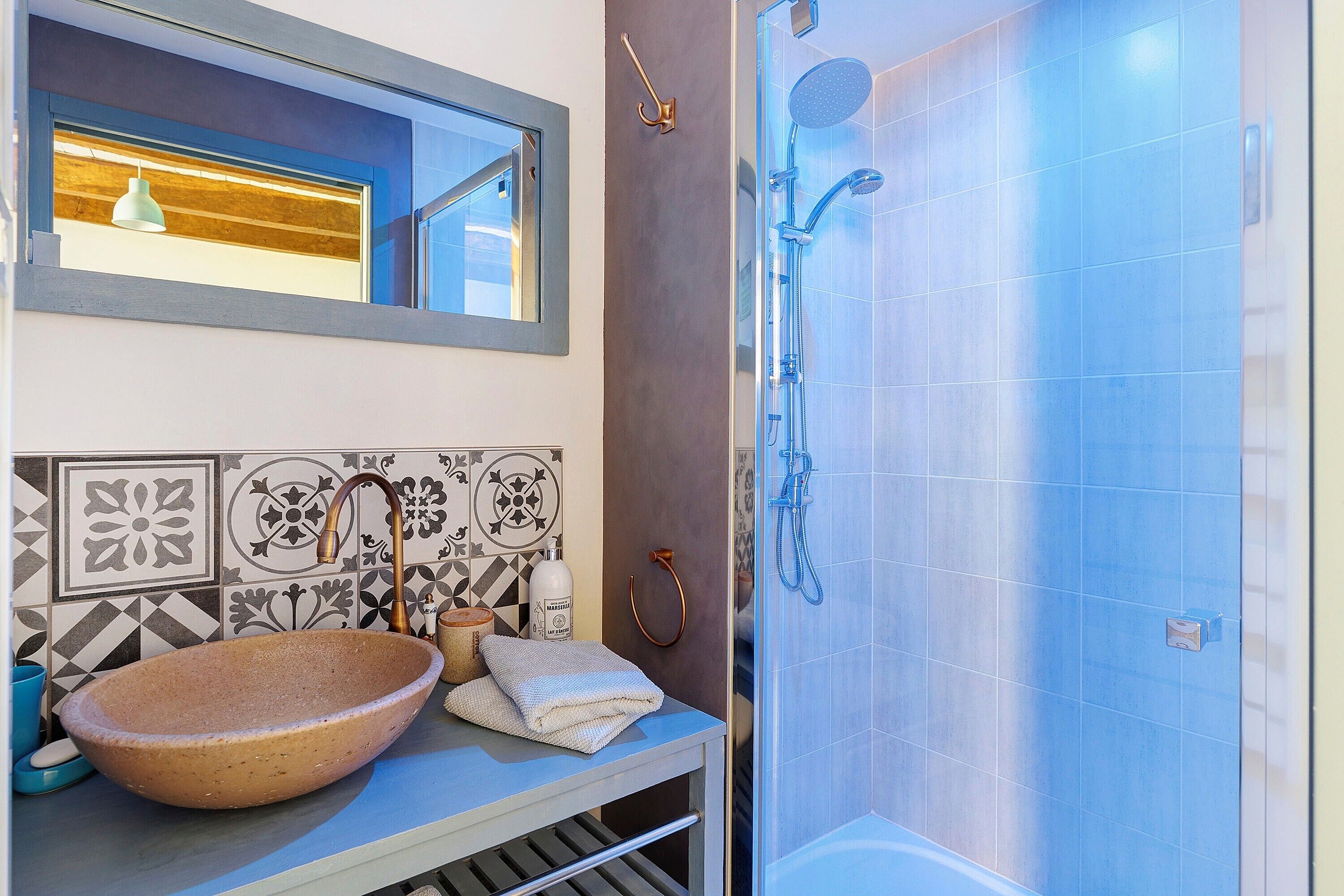 A bathroom with a large vessel sink, a mirror, a shower with a handheld showerhead, and patterned tiles on the wall.