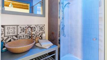 A bathroom with a large vessel sink, a mirror, a shower with a handheld showerhead, and patterned tiles on the wall.