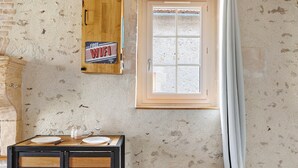 A rustic room with a wooden table set for two, a window with a view, and a wall-mounted Wi-Fi sign. - Holiday Home “Le Gîte Aïdan” with Shared Garden and Wi-Fi (LA PUYE)