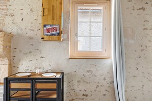 A rustic room with a wooden table set for two, a window with a view, and a wall-mounted Wi-Fi sign. - Holiday Home “Le Gîte Aïdan” with Shared Garden and Wi-Fi (LA PUYE)