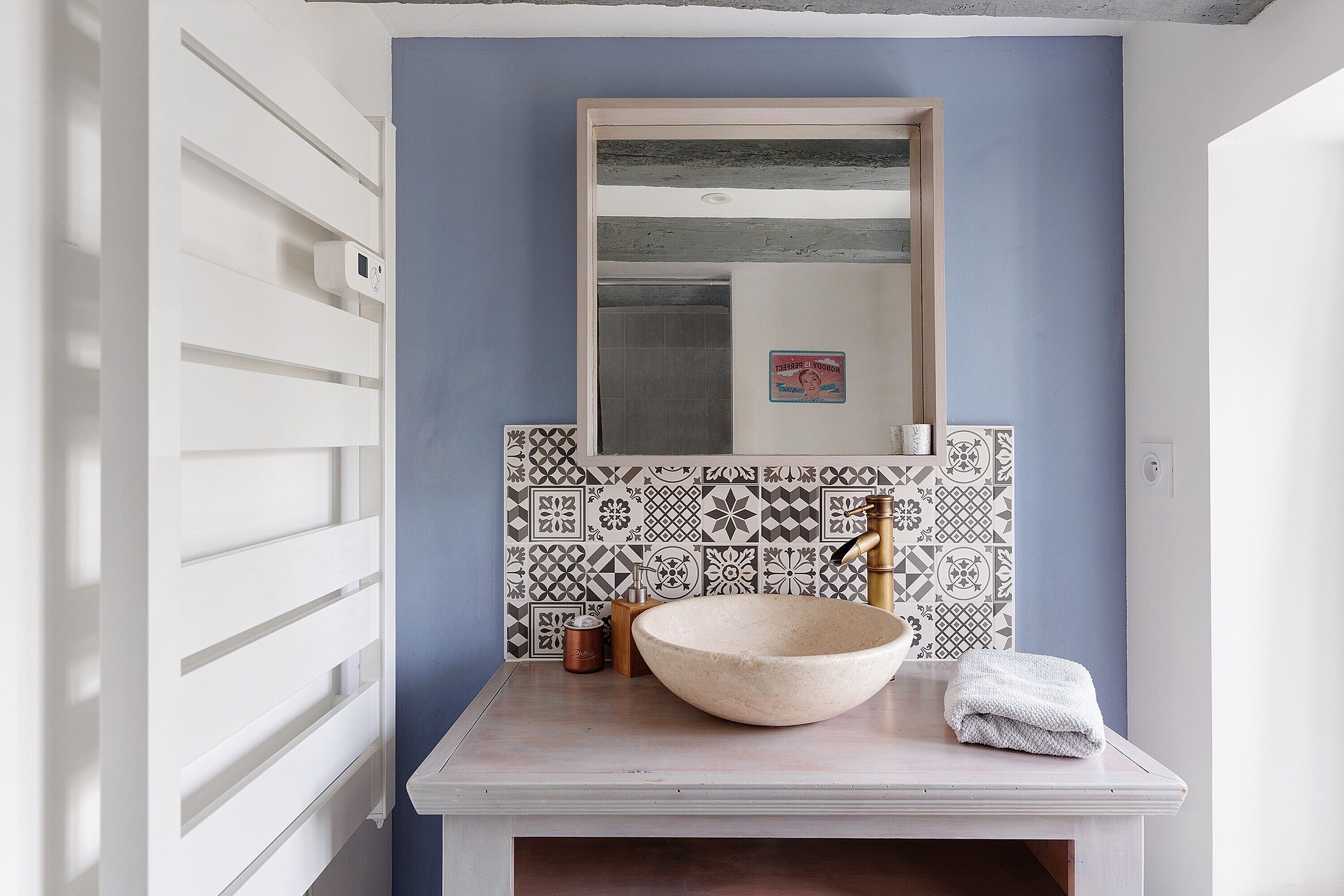 A bathroom with a white sink, a large mirror, and patterned tiles.