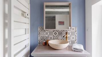 A bathroom with a white sink, a large mirror, and patterned tiles.