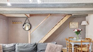 Ein Zimmer mit grauem Sofa, einem Holzesstisch und Stühlen, einer Holztreppe und einem an der Wand befestigten Spiegel.