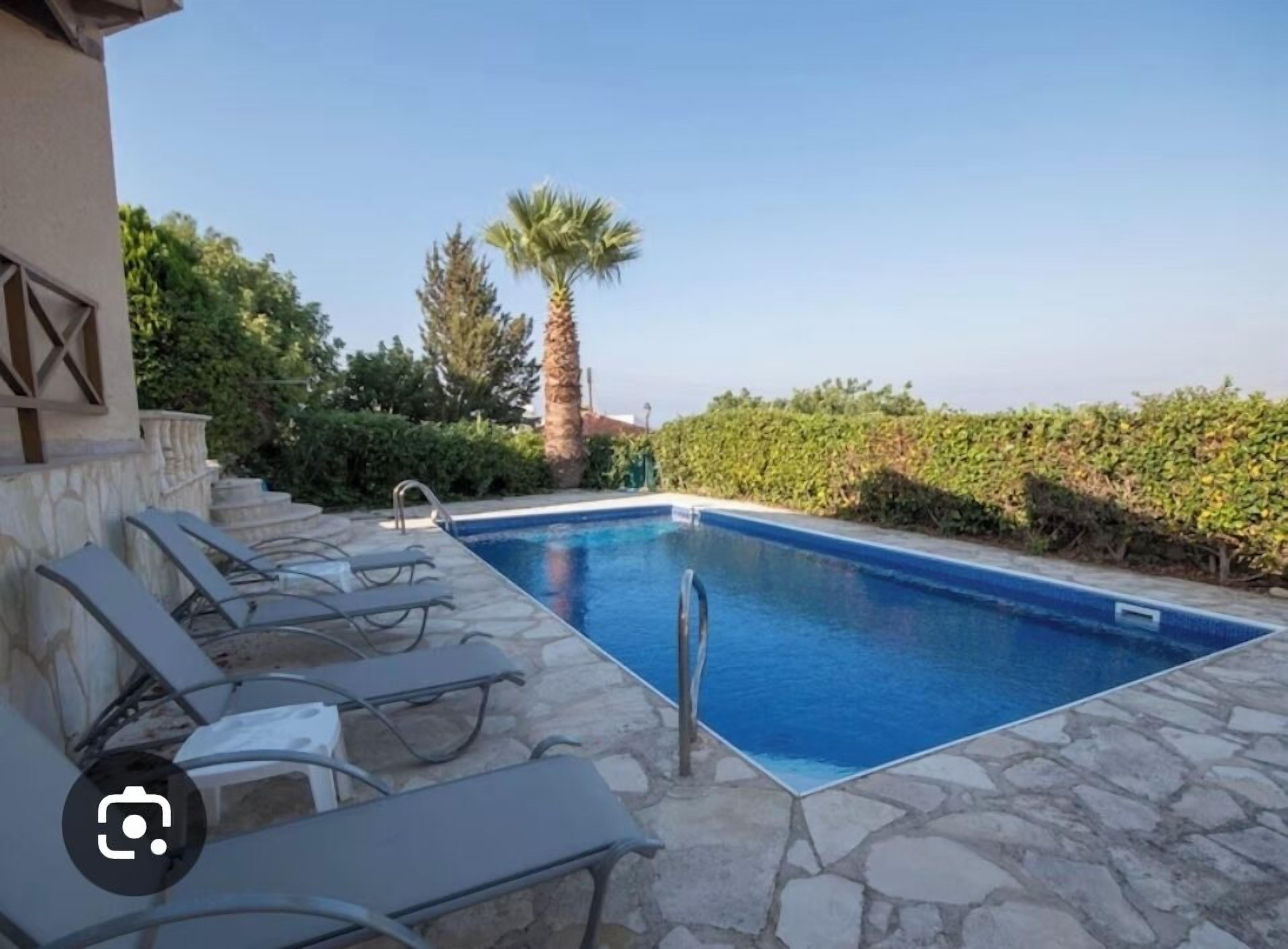 A swimming pool with lounge chairs, stone flooring, and a clear sky.