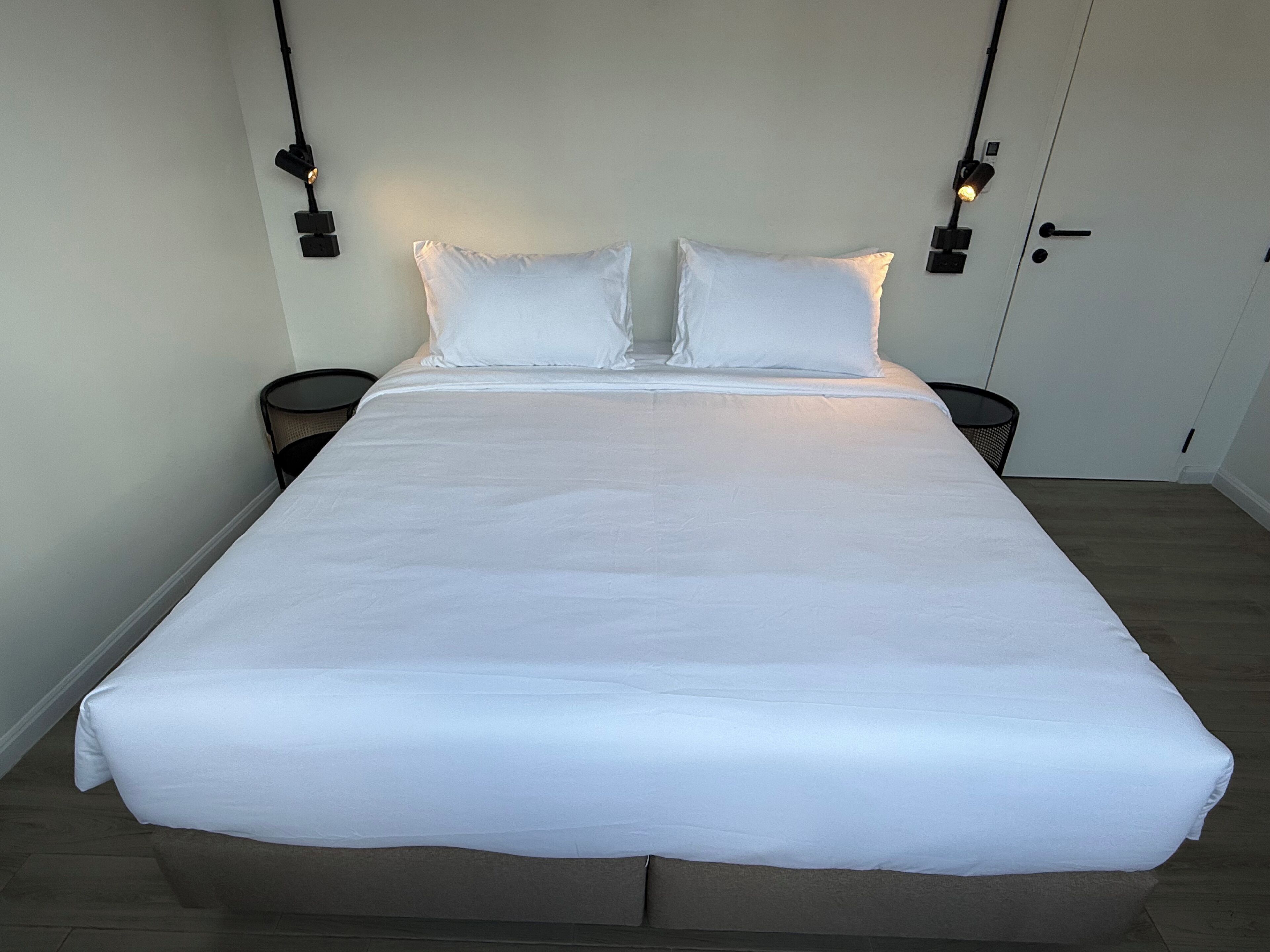 A large bed with white linens, two bedside tables, and a door with a handle.