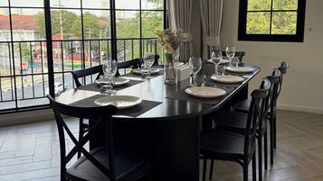 A dining area with a large table set for six, surrounded by black chairs, large windows with curtains, and a view of the cityscape.