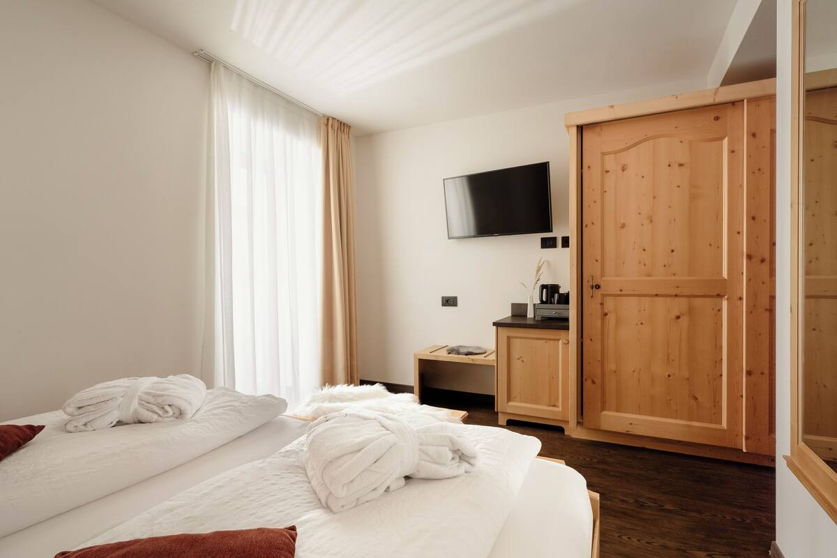 A hotel room with two beds, a TV mounted on the wall, and a wooden wardrobe.
