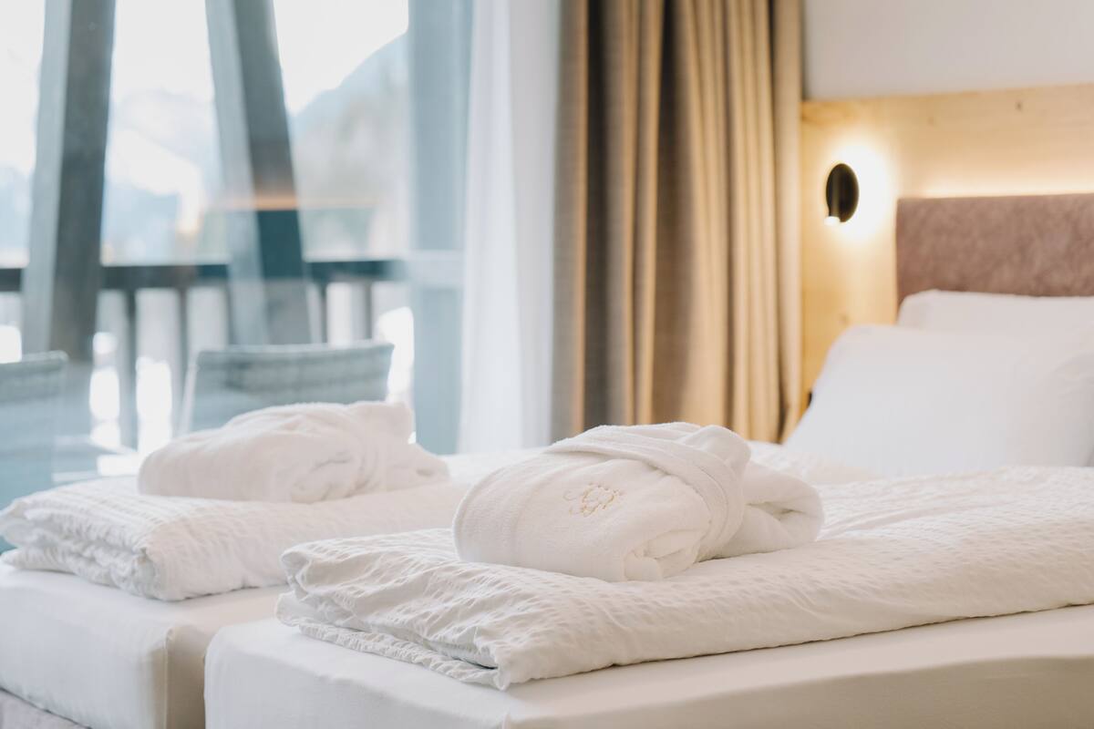 A hotel room with a bed, white towels, a headboard, and a window with curtains.