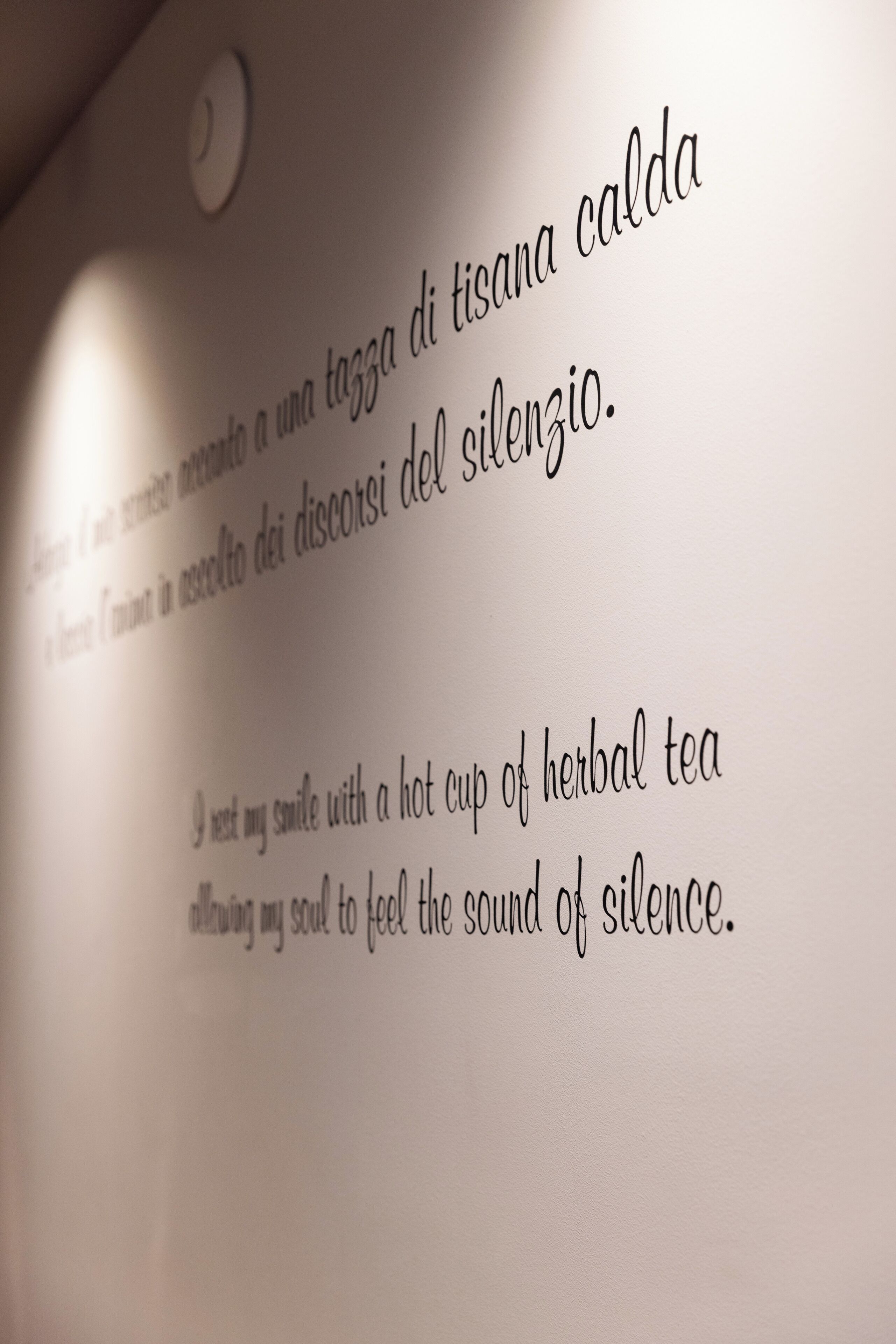 A close-up of a wall with text in Italian, possibly a quote or a poem, and a light fixture above it.