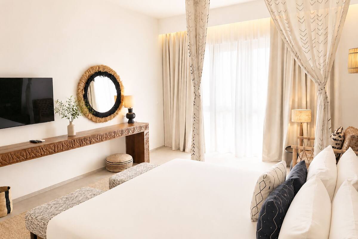 A hotel room with a large bed, a TV, a mirror, a console table, and a window with curtains.