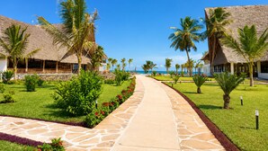 Un resort con edificios de techo de paja, palmeras y un camino pavimentado.