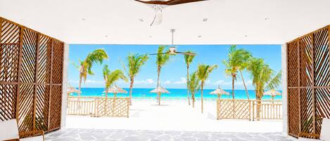 A room with a beach view, a ceiling fan, stone flooring, and wooden partitions.