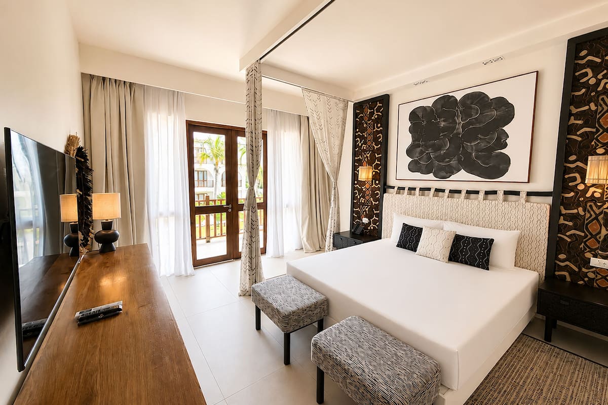 A hotel room with a large bed, a desk with a lamp, a television, and a view of the outside.