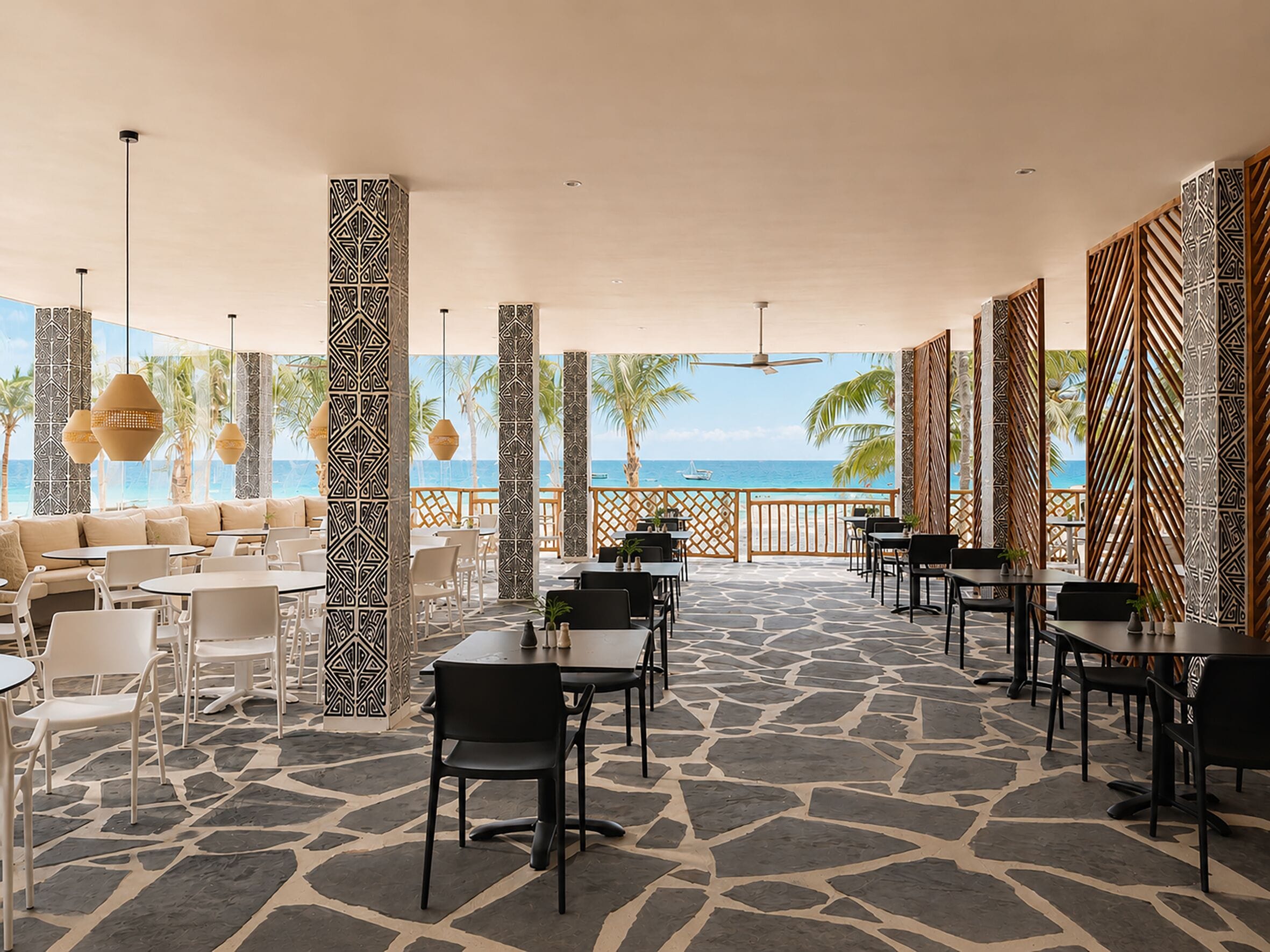 A covered outdoor seating area with tables and chairs, patterned columns, and a view of the ocean.