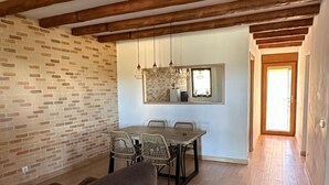 Ein geräumiger Wohnbereich mit Holzbalkendecke, Backsteinwand, Esstisch mit Stühlen und einer Couch.