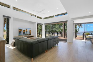 Ein modernes Wohnzimmer mit einer Eckcouch, einem Flachbildfernseher und großen Fenstern mit Blick ins Freie.