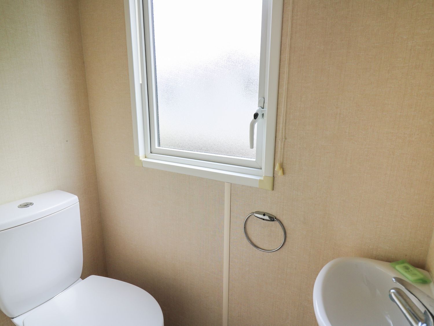 Een kleine badkamer met toilet, raam en wastafel.