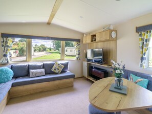 Ein gemütliches Wohnzimmer mit Sofa, Fernseher, einer Holzkommode und Blick ins Freie.