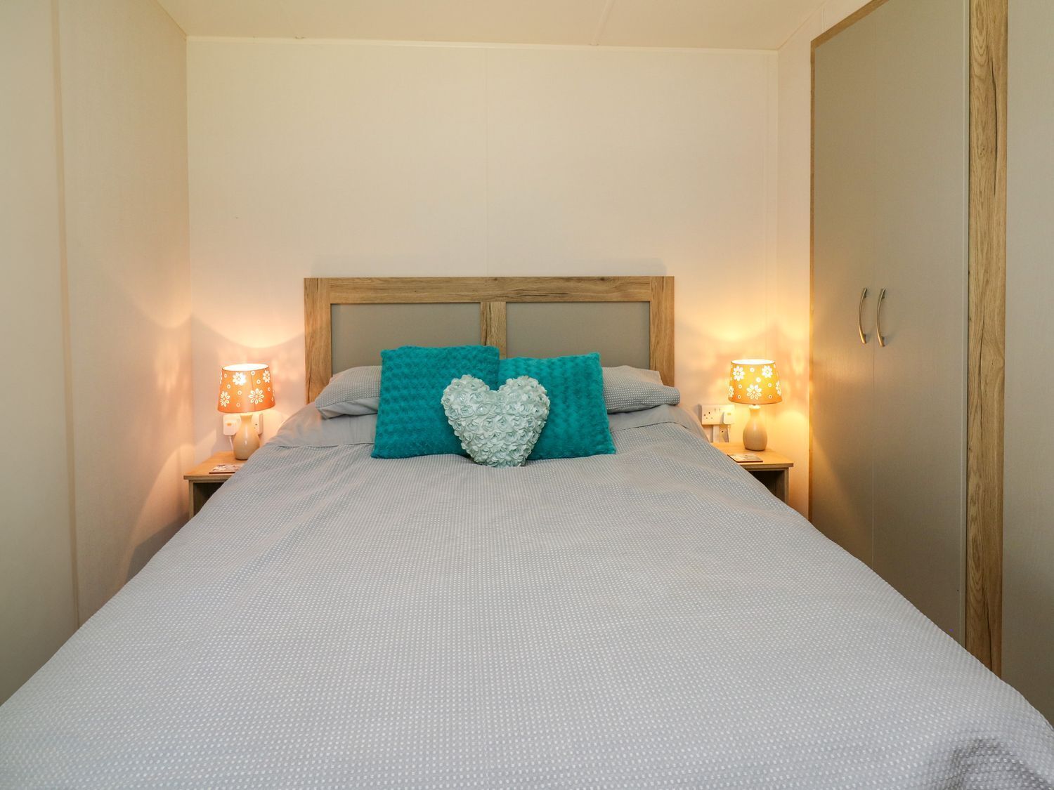 A neatly made bed with a wooden headboard, two bedside lamps, and a heart-shaped pillow.