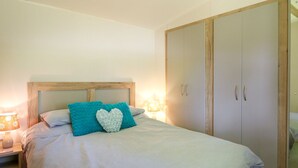 A neatly made bed with a wooden headboard, a nightstand with a lamp, and a wardrobe with two doors. - Caravan 6 at Blackmoor Farm Near Tenby (Narberth)