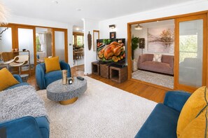 A modern living room with a blue sofa, a coffee table, and a television displaying a roasted turkey. - Famous Palm Beach Home! 120-jet Spa Cabana, Games Room & Prime Central Location! (Sydney)