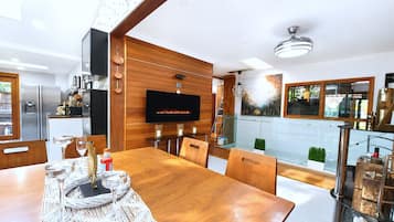 A modern kitchen with a flat-screen TV, wooden cabinetry, and a dining area with a wooden table and chairs.