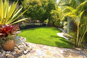 A well-maintained garden with a stone pathway, lush green lawn, and various tropical plants.