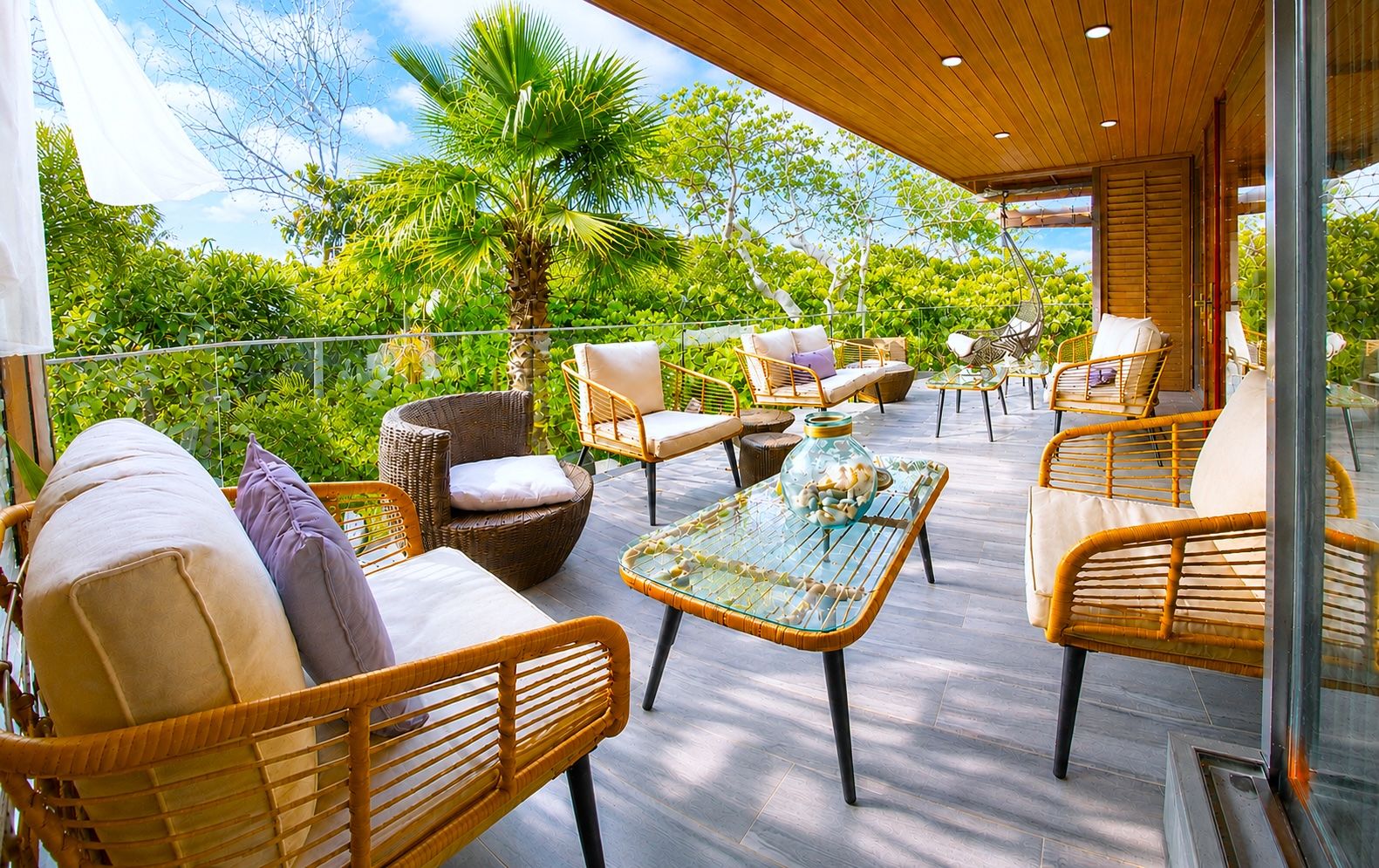 An outdoor seating area with wicker furniture, a glass-top table, and a view of lush greenery.