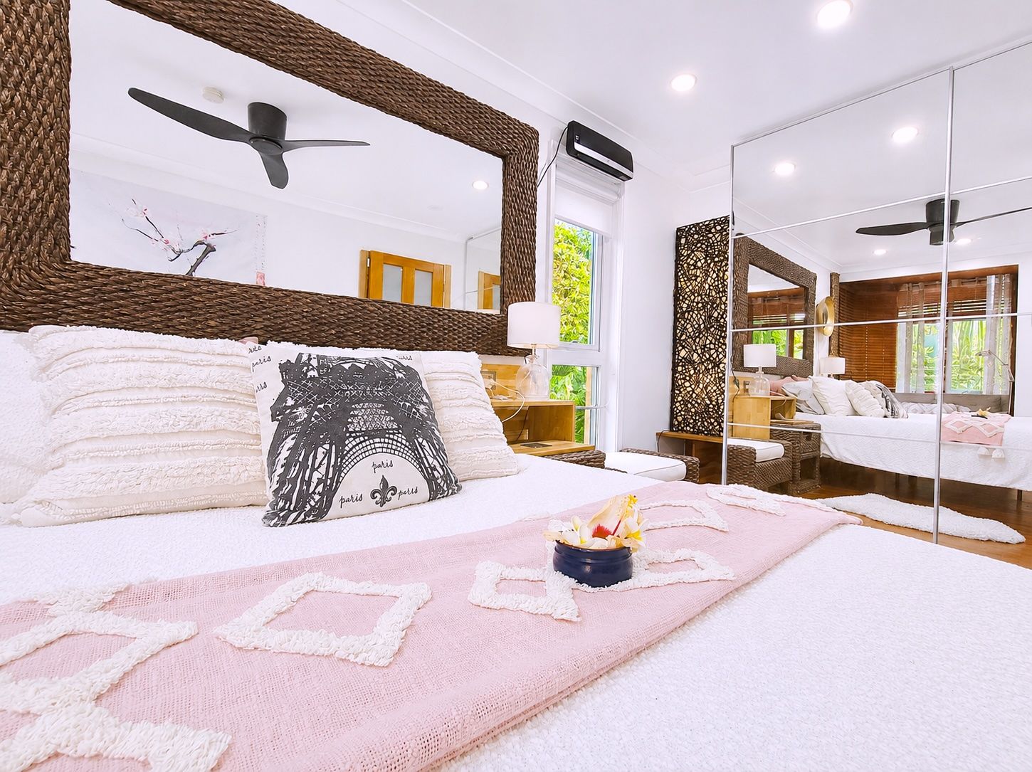 Un dormitorio moderno con una cama grande, un ventilador de techo y vistas al exterior a través de una ventana.