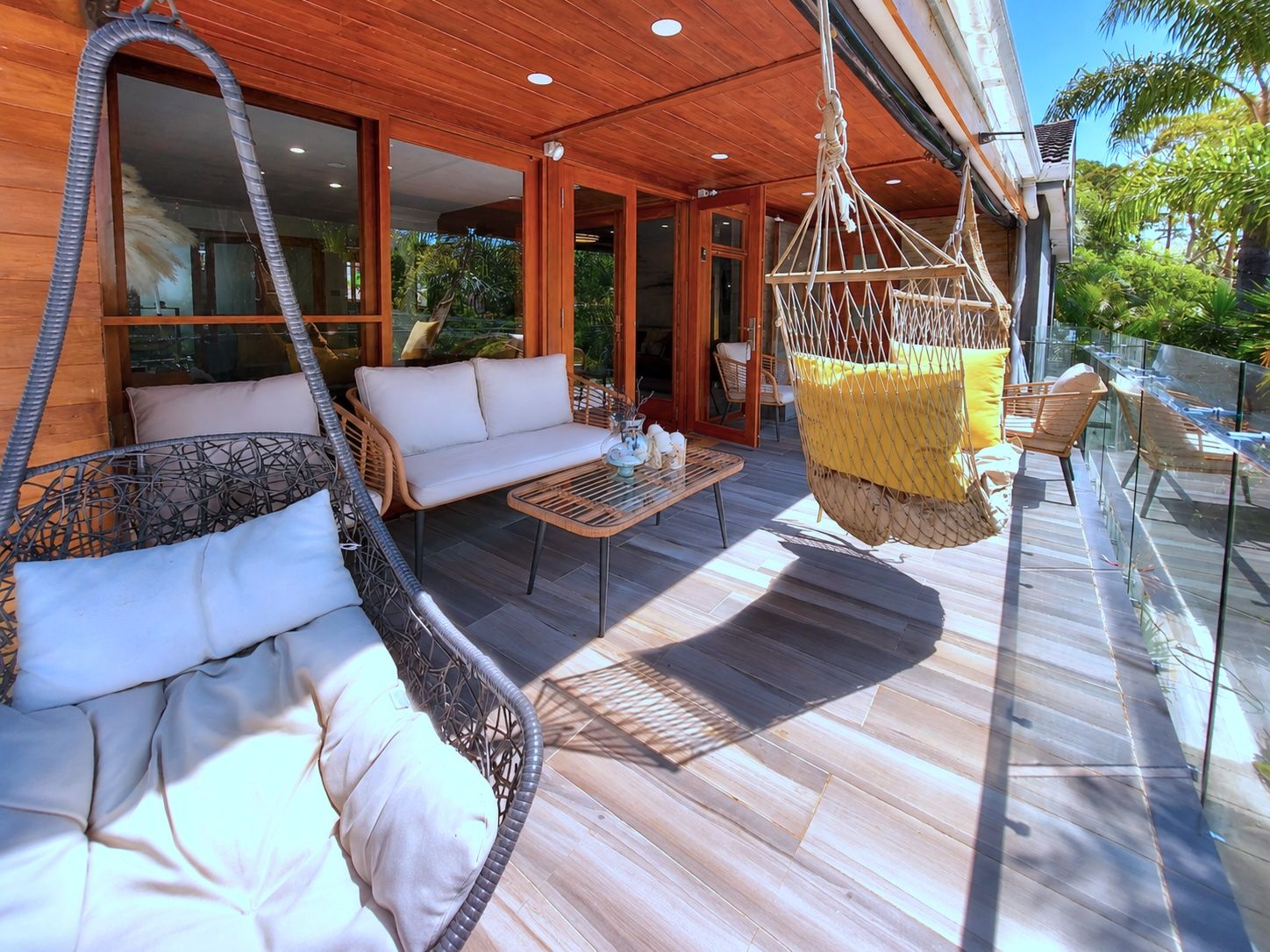 A covered outdoor seating area with wicker furniture, a hanging chair, and a wooden ceiling.