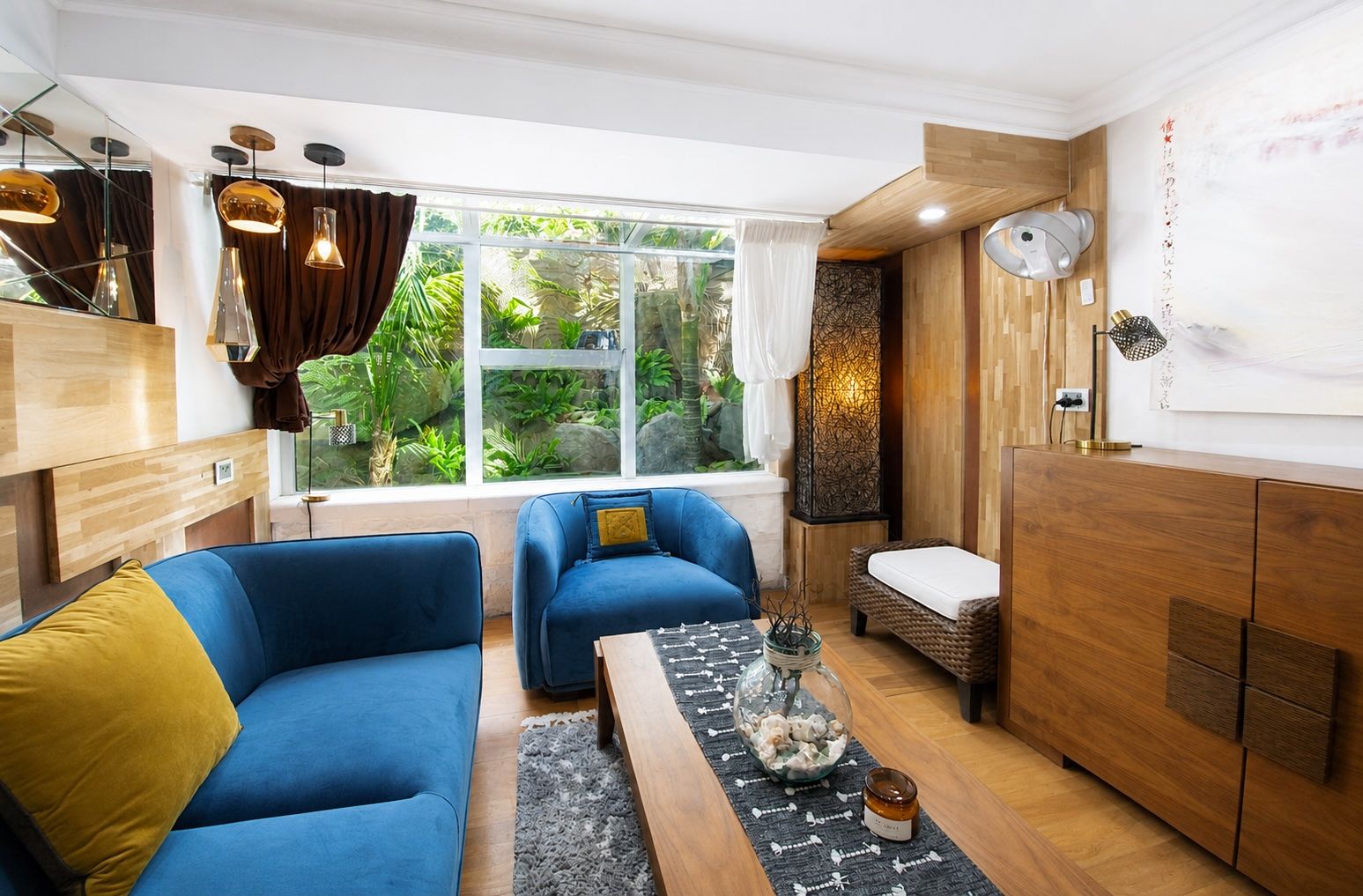 A modern living room with a sofa set, a coffee table, and a view of greenery through a large window.