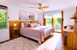 A bedroom with a bed, a ceiling fan, a large window, and a view of greenery outside. - Famous Palm Beach Home! 120-jet Spa Cabana, Games Room & Prime Central Location! (Sydney)