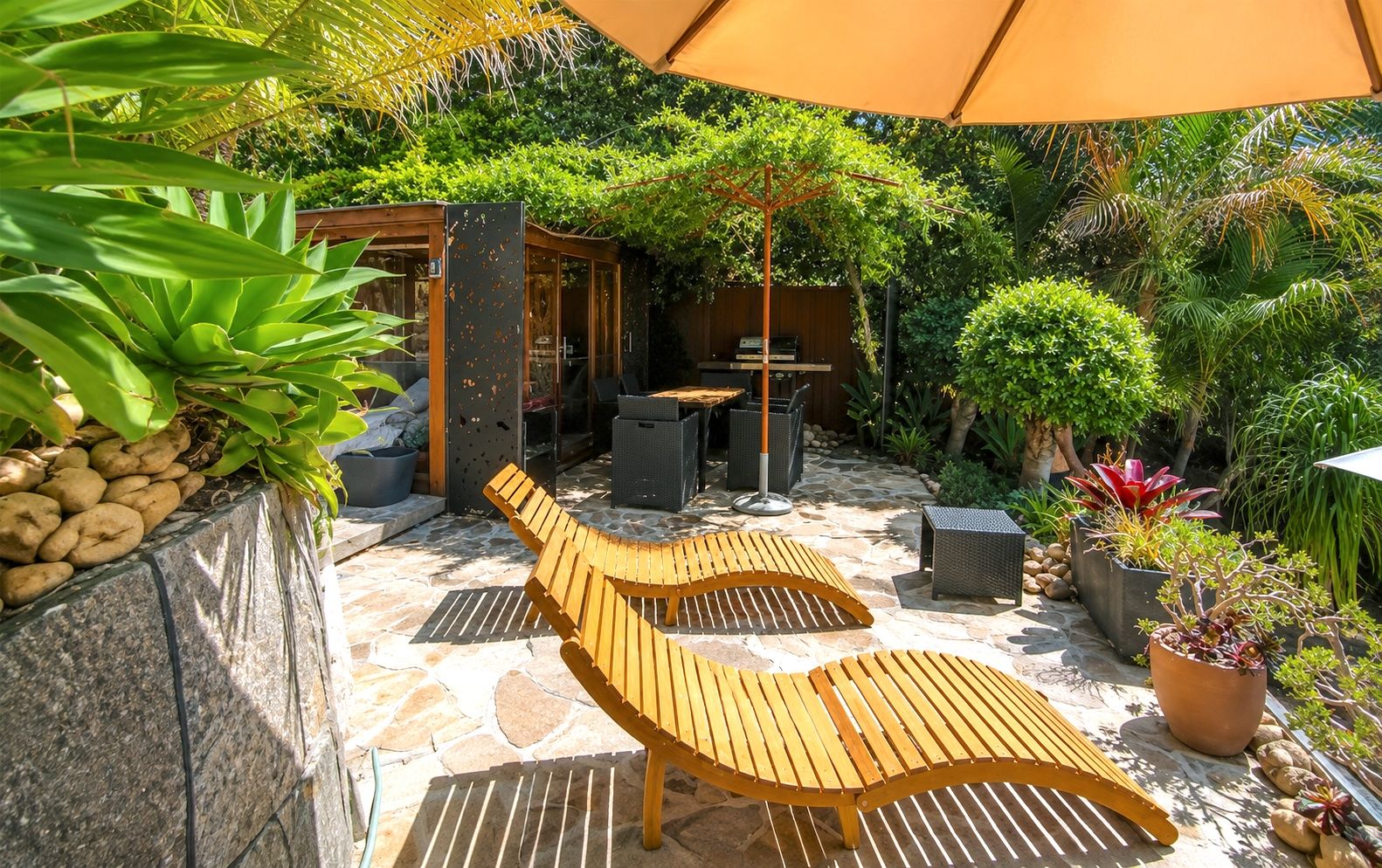 Eine Terrasse mit Holztisch und -stühlen, Steinboden und Kübelpflanzen.