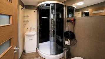 A modern bathroom with a glass-enclosed shower, a sink, and a hairdryer mounted on the wall.