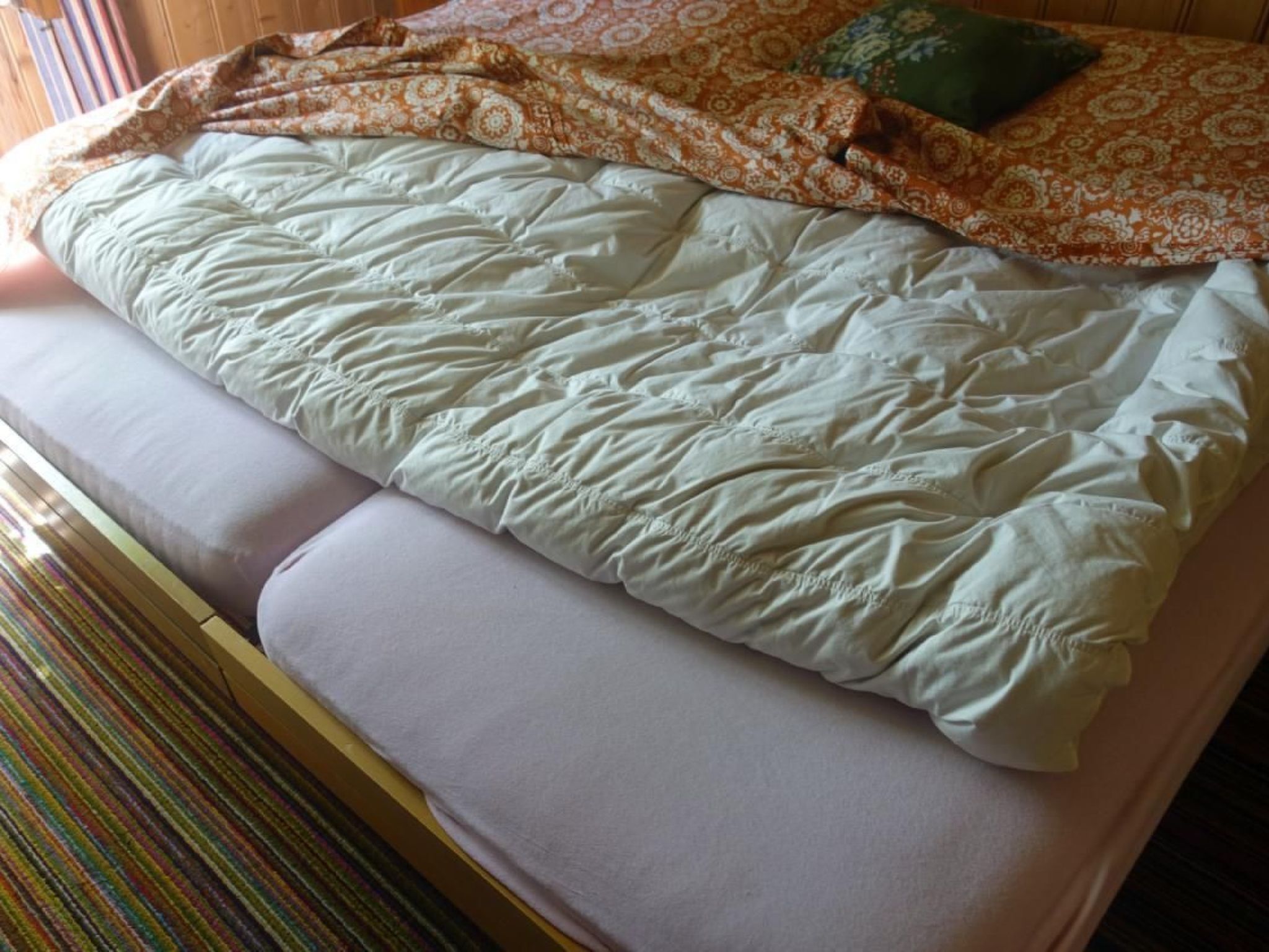A bed with a patterned blanket and pillows, a striped rug, and a wooden headboard.