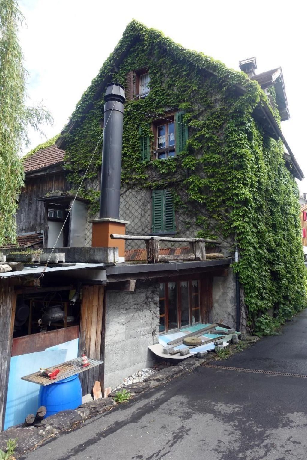Ein Haus mit Schornstein, einem blauen Fass und einer Holzkonstruktion.