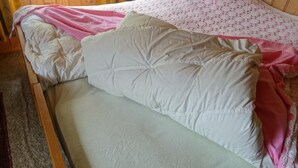 Ein Bett mit weißem Kopfkissen, einer grünen Matratze, einer rosa Decke und einem Spitzenüberwurf.